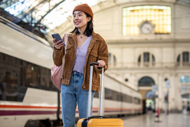 istock A young beautiful Chinese woman is using a mobile phone at a train station while waiting to enter a train car, checking which platform her train is on via a mobile app 1785565879