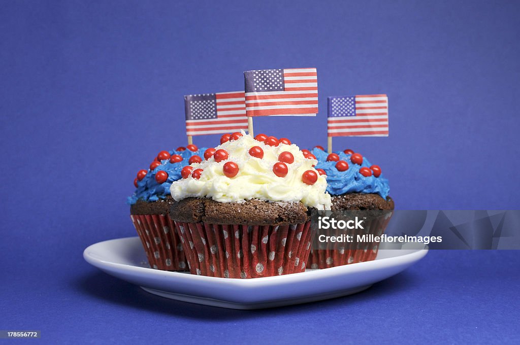 Fourth 4th of July party cupcakes. Fourth 4th of July, Independance Day, party celebration with red, white and blue chocolate cupcakes on white heart plate and USA American flags Cake Stock Photo