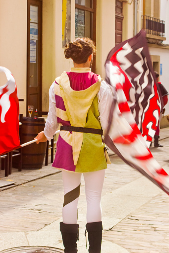 Rear view of street artist flag performer  in medieval costume, parade. Mondoñedo medieval historical reenactment. Lugo province, Galicia, Spain.