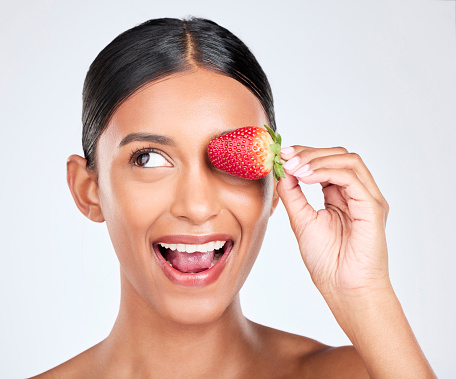 Health, smile and woman with a strawberry in studio for healthy diet snack for nutrition. Wellness, beauty and young Indian female model with fruit for natural skin detox routine by white background.