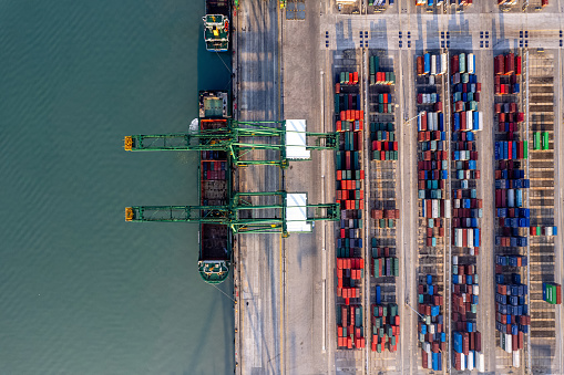 Aerial view of a heavy loaded container cargo vessel traveling over calm, blue sea