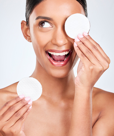 Face, happy woman and cotton pad, beauty and makeup removal with skincare and clean on white background. Hygiene, excited for cosmetics and product with wellness, dermatology and skin shine in studio