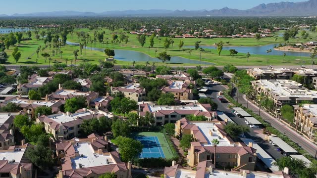 Southwest USA aerial view: lush golf courses, water features, and terracotta-roofed residences, with mountain backdrop and clear blue skies.