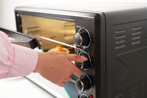 Woman's hands taking buscuit cupcakes out of mini oven closeup