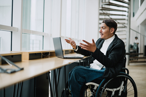 Asian Malay wheelchair businessman having online meeting in office.