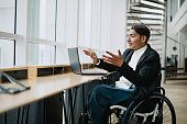 Asian Malay wheelchair businessman having online meeting in office.