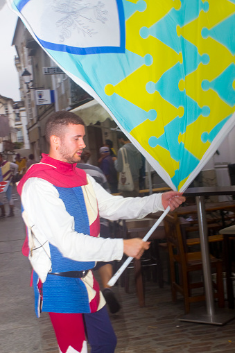 Street artist flag male performer  in multi colored medieval costume, parade. Mondoñedo medieval historical reenactment. Lugo province, Galicia, Spain.