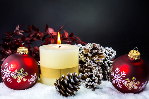 Christmas candle in a recycled glass jar on the table with fir branches, christmas lights and ornaments. Home window at the background