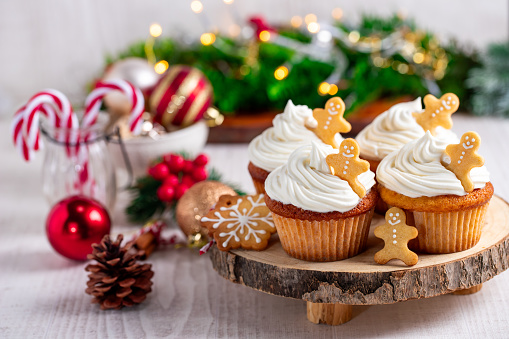 Cupcakes with gingerbread cookies and christmas lights on a white wooden table