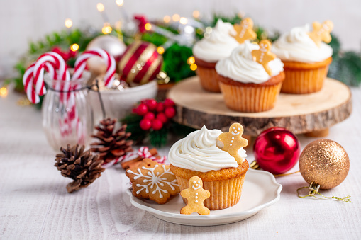 Cupcakes with gingerbread cookies and christmas lights on a white wooden table