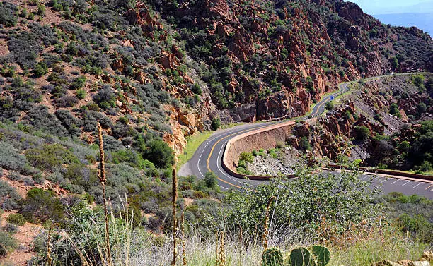 "Curving mountain road winds its way to Jerome, Arizona.  Red rocky cliffs overhand highway."