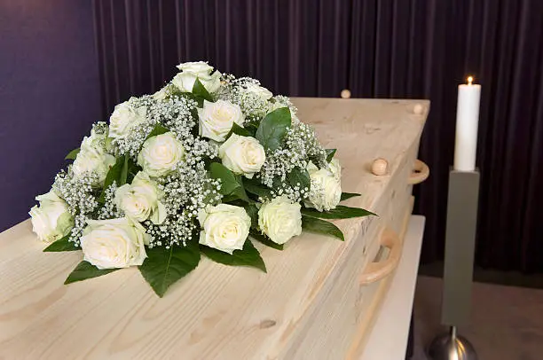 A flower arrangement on a coffin and a burning candle on the background in a mortuary
