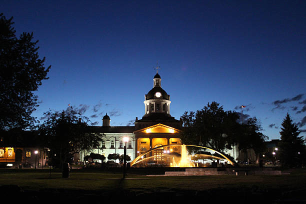 City Hall and Confederation Basin Fountain in Kingston, Ontario Canada Night photo showing an illuminated City Hall in Kingston Ontario Canada.  In front of the domed clock tower, is a fountain in Confederation Basin park, also lit up at night.  The photo was taken from the water.  The fully restored City Hall is amazing historical architecture. kingston ontario photos stock pictures, royalty-free photos & images