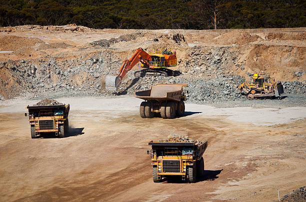 Busy Mine This is a mine showing three large trucks driving to and from a bulldozer and digger which fill them with rock ore. This shot was taken at the Galaxy Lithium mine in Ravensthorpe, Western Australia. open pit mine stock pictures, royalty-free photos & images