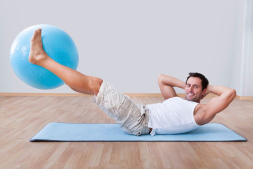 Young Man Exercising On A Pilates Ball, Indoors