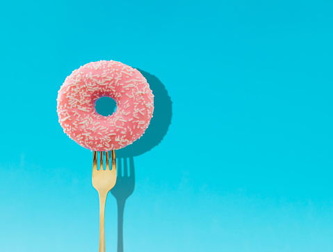 Yummy pink glazed donut pricked on a fork on bright light blue background. Creative art. Contemporary style. Minimal concept of food with copy space. Donut aesthetic background.