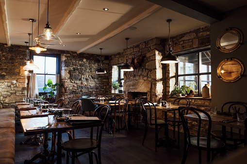 A wide shot of a rustic gastro pub located in Northumberland. The restaurant is empty, ready for customers with glasses, menus, knives, and forks on the tables. The pub is Located in Seahouses, Northumberland.