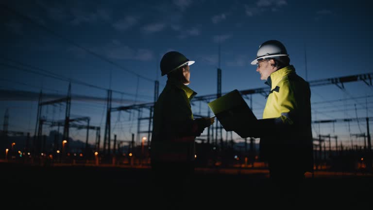 SLO MO Electrical Engineers Discussing While Holding Laptop And Digital Tablet At Dark Power Station During Night