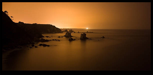 Night Photography with little moon on the beach of silence in Asturias. The light that is seen in the background is the beacon of Ovid that was filling the whole scene