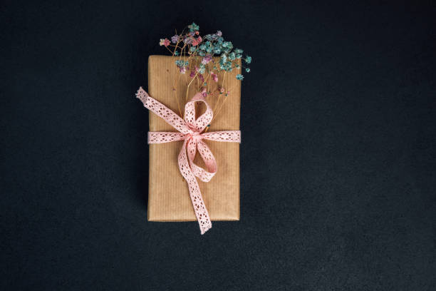 Background for greetings. Gifts wrapping in soft pink paper with dry flowers on a black concrete background stock photo
