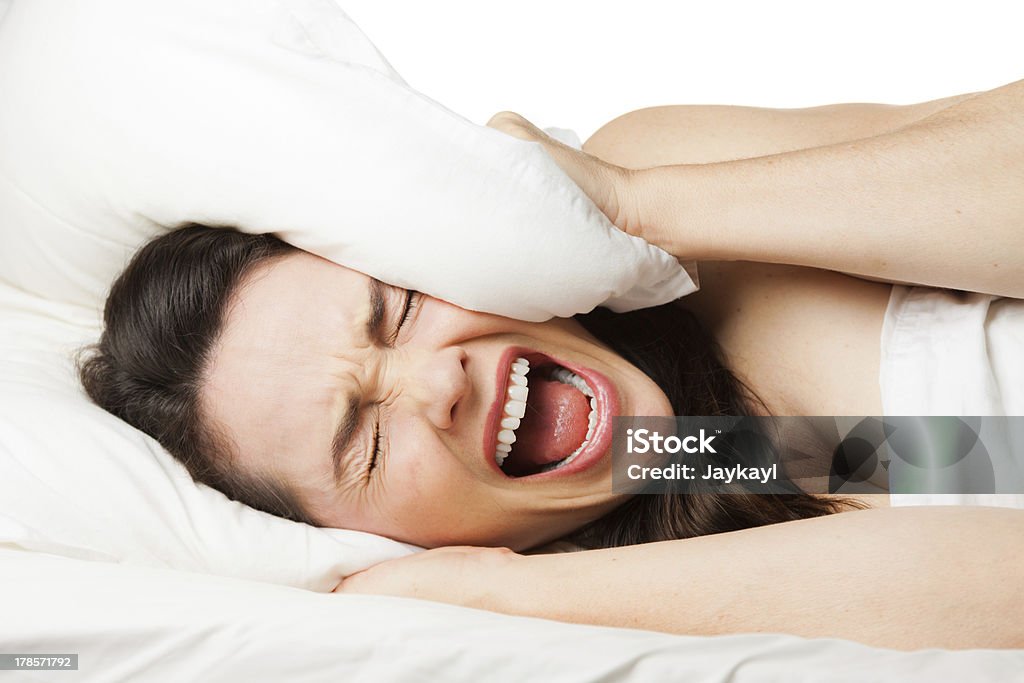 Frustrated woman trying to sleep A frustrated tired woman hides her head in her pillow and screams beacuse she can't sleep. Isolated on white. Bedroom Stock Photo