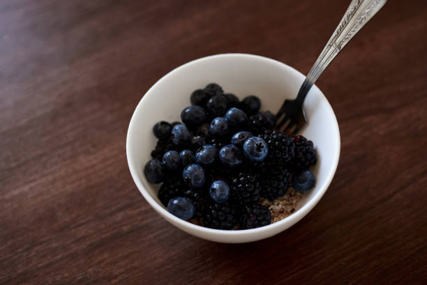 A white bowl filled with dark blue blackberries and blueberries isolated on brown wooden table. Healthy nutrition ration. Fruit and vegetable diet. Raw food. Eat healthy, keep fit.