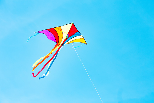 Rainbow kite flying in blue sky in sunny day in summer. Childhood concept.