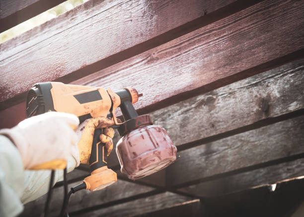 Two hands with gloves holding corded stain gun to repaint pergola timer wood outdoor structure in redwood color, residential house renovation remodel DYI project in Dallas, Texas, USA. Red Cedar dos manos con guantes sosteniendo una pistola de tinte con cable para volver a pintar la estructura exterior de madera del temporizador de la pérgola en color secuoya, proyecto de remodelación de renovación de casas residenciales dyi en dallas, texas, e
