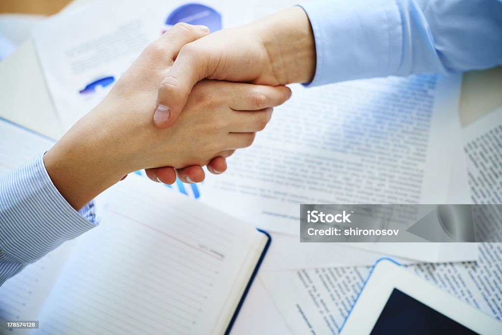 Business deal Close-up of female and male handshaking over workplace with business documents Agreement Stock Photo