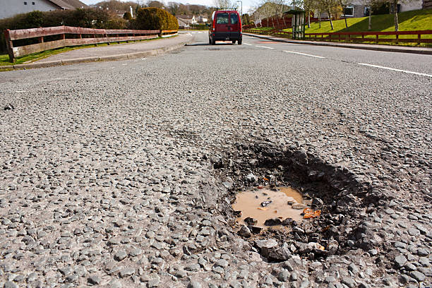 Pot hole in residential road surface Large deep pothole an example of poor road maintance due to reducing local council repair budgets sinkhole stock pictures, royalty-free photos & images