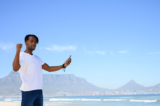 Gay black man holding phone on beach