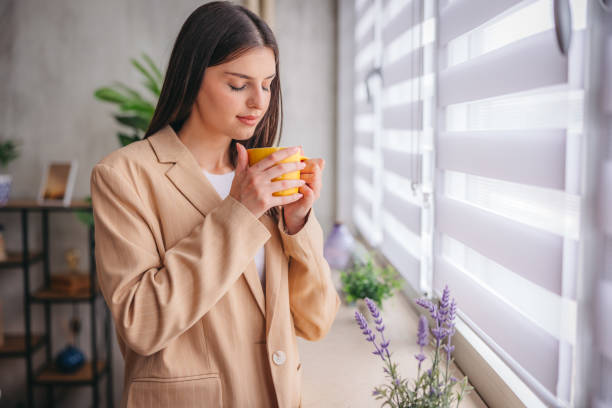 istock Young woman holding a cup of coffee while looking out the window 1785773112