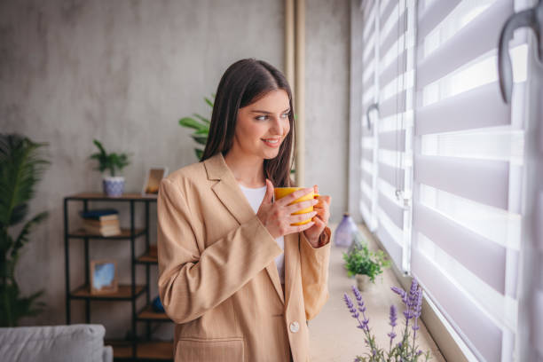 istock Young woman holding a cup of coffee while looking out the window 1785773113