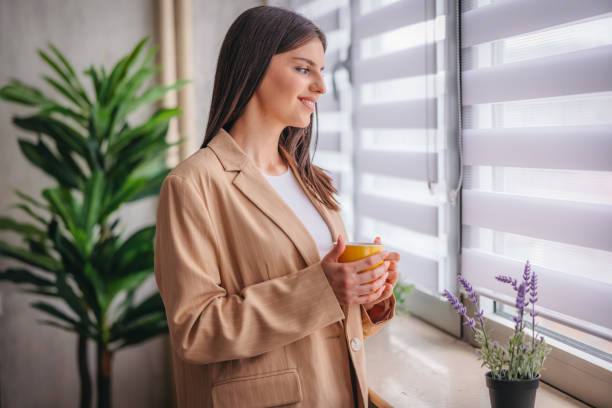 istock Young woman holding a cup of coffee while looking out the window 1785773114