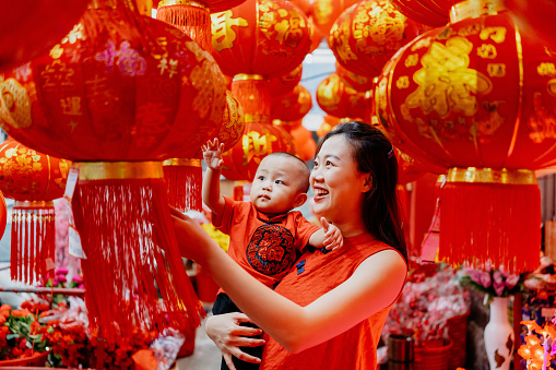 An Asian Chinese mother carrying her baby shopping and looking for red lantern for Chinese new year decoration