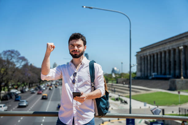 istock Non-binary person looking at camera while raising a fist and holding smart phone in Buenos Aires 1785792026