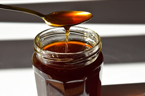A jar of honey being scooped with a spoon, placed on top of a white kitchen table
