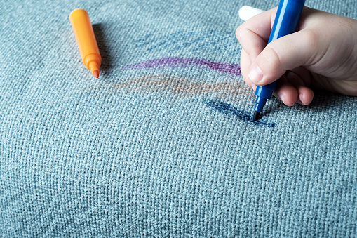 Children hand drawing a blue felt-tip pen on the fabric sofa