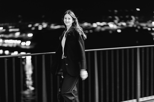Businesswoman walking at the street, night city. Female portrait of woman outdoors, person wear business clothing. Blurred background, bokeh with lights. Black and white photography.