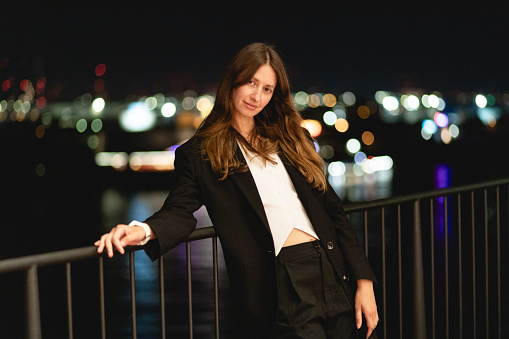 Businesswoman walking at the street, night city. Female portrait of woman outdoors, person wear business clothing. Blurred background, bokeh with lights.