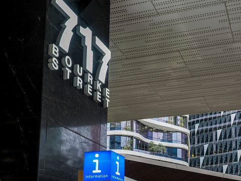 Melbourne, Australia - Aug 29, 2022: 717 Bourke Street and blue Information signs decorate a black marble pillar. These elements frame the modern architectural design of a distant building.