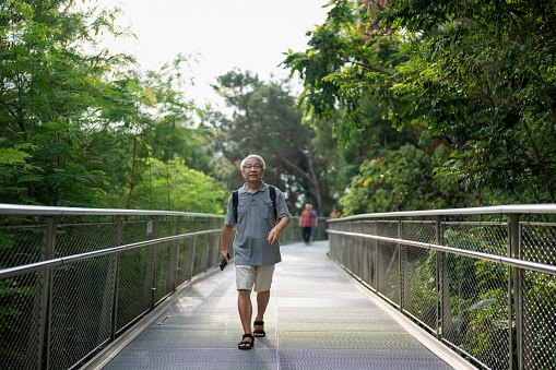 Asian old man hiking on footbridge in park