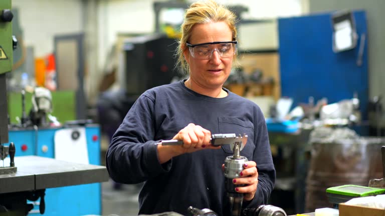 Female factory worker operator working in numerical control sector measuring drill bits, industrial factory