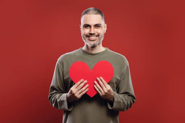 man smiling, holding a paper heart with both hands - human heart flash imagens e fotografias de stock