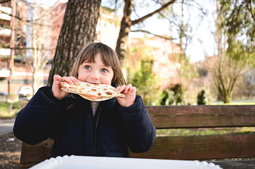 Preschool child eating flatbread sitting in a parkland.