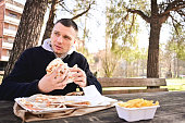 young man eating sandwich outdoors in a park.