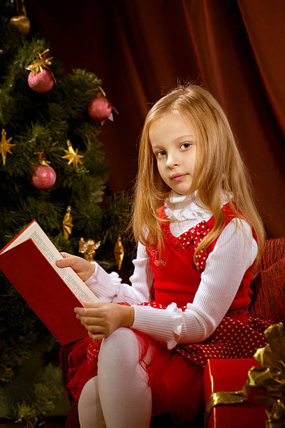 little blonde girl reading book near Christmas tree stock photo