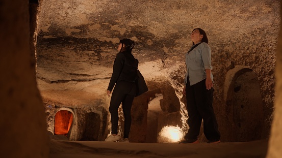 Two female tourist friends are visiting an underground city in Cappadocia Türkiye Turkey during their travel.