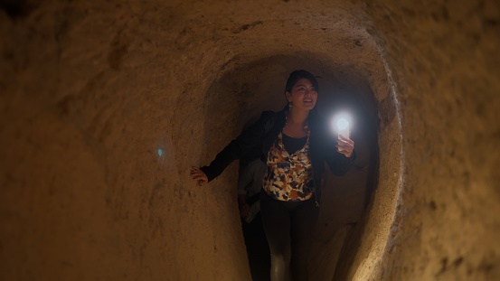 A multiracial female tourist is visiting an underground city and using her smart mobile phone to take photos and videos in Cappadocia Türkiye Turkey during her travel.