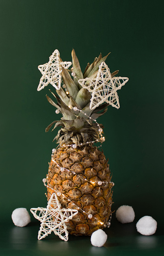 Christmas decor concept with pineapple, balls, white stars and artificial snowballs on green background. Copy space